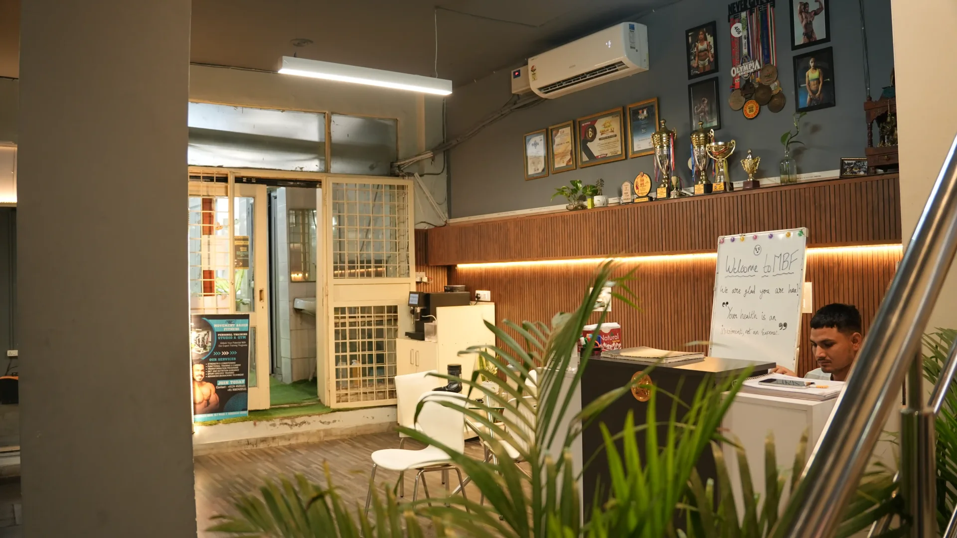 Reception area with welcome board, trophies, and indoor plants